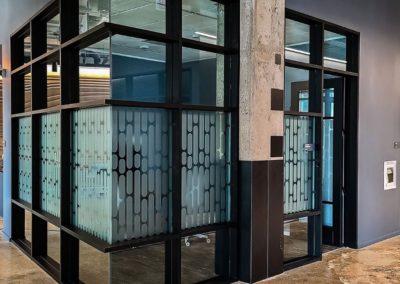 Interior glazed partition with frosted glass panels in dark aluminum framing, next to a concrete column