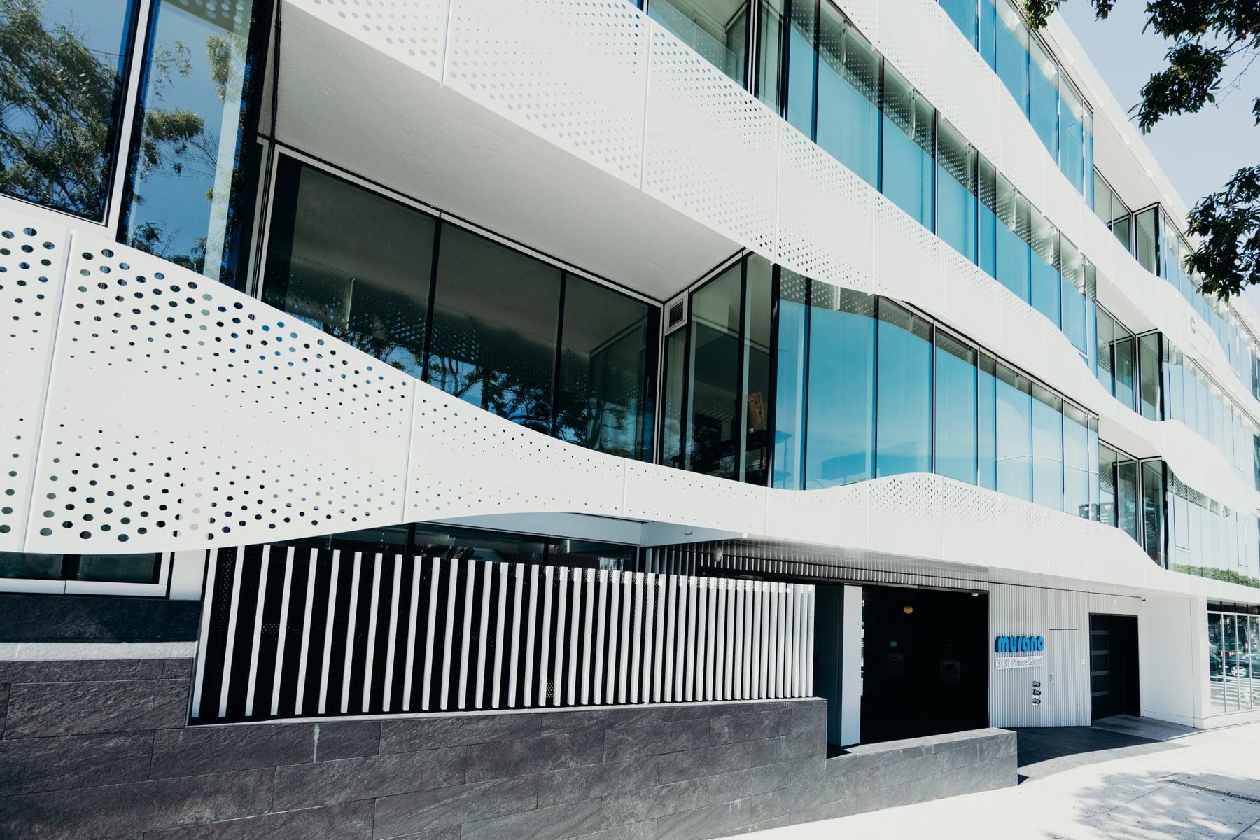Entrance of The Murano with a white perforated metal panel curving along the facade above glazing