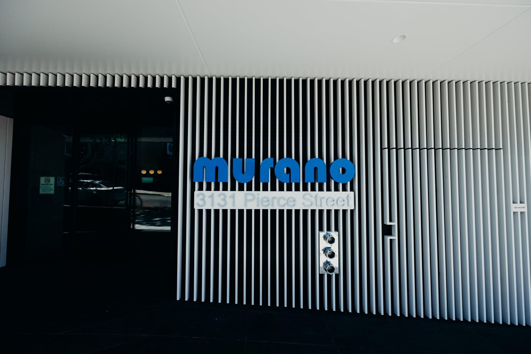 Blue Murano sign on a white vertical-fin entrance wall