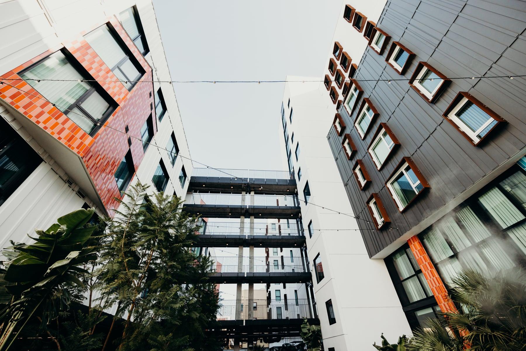 Courtyard between buildings with orange tile cladding, dark metal siding with orange-framed windows and walkways crossing overhead