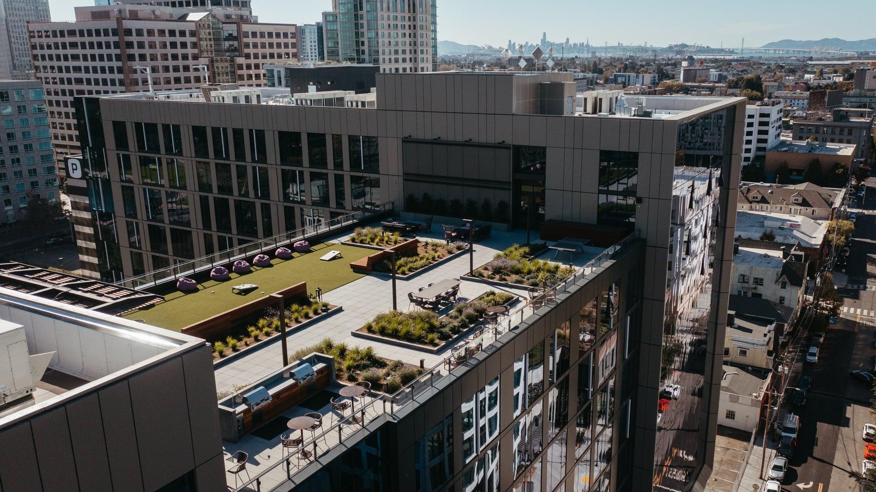 Rooftop terrace with planting beds and lawn on a tall Oakland building, with the city beyond