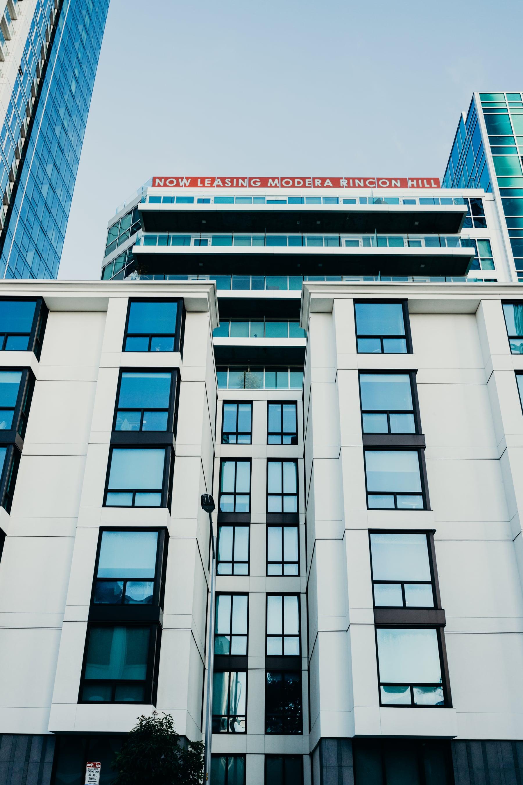 White building facade with rows of dark-framed windows and a leasing sign at the roofline
