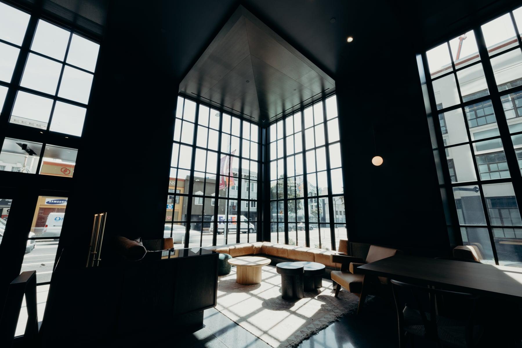 Lobby lounge with tall black-framed glazed bays, seating and sunlight on the floor