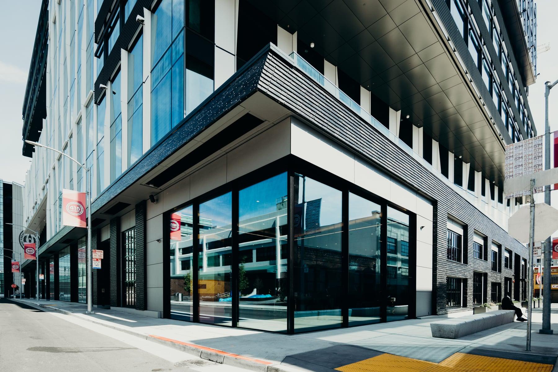 Street corner at 415 Natoma with a black-framed glass storefront below a dark metal soffit