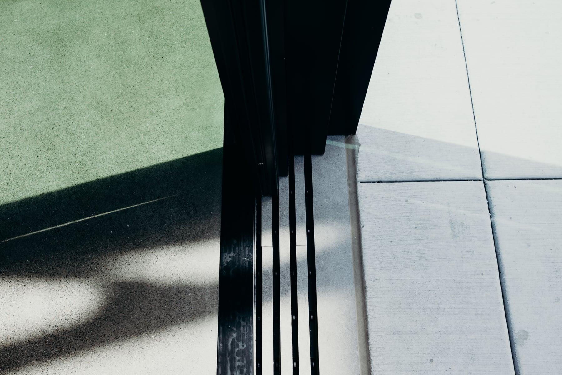 Close view of a black metal door frame and its bottom track at the sidewalk threshold