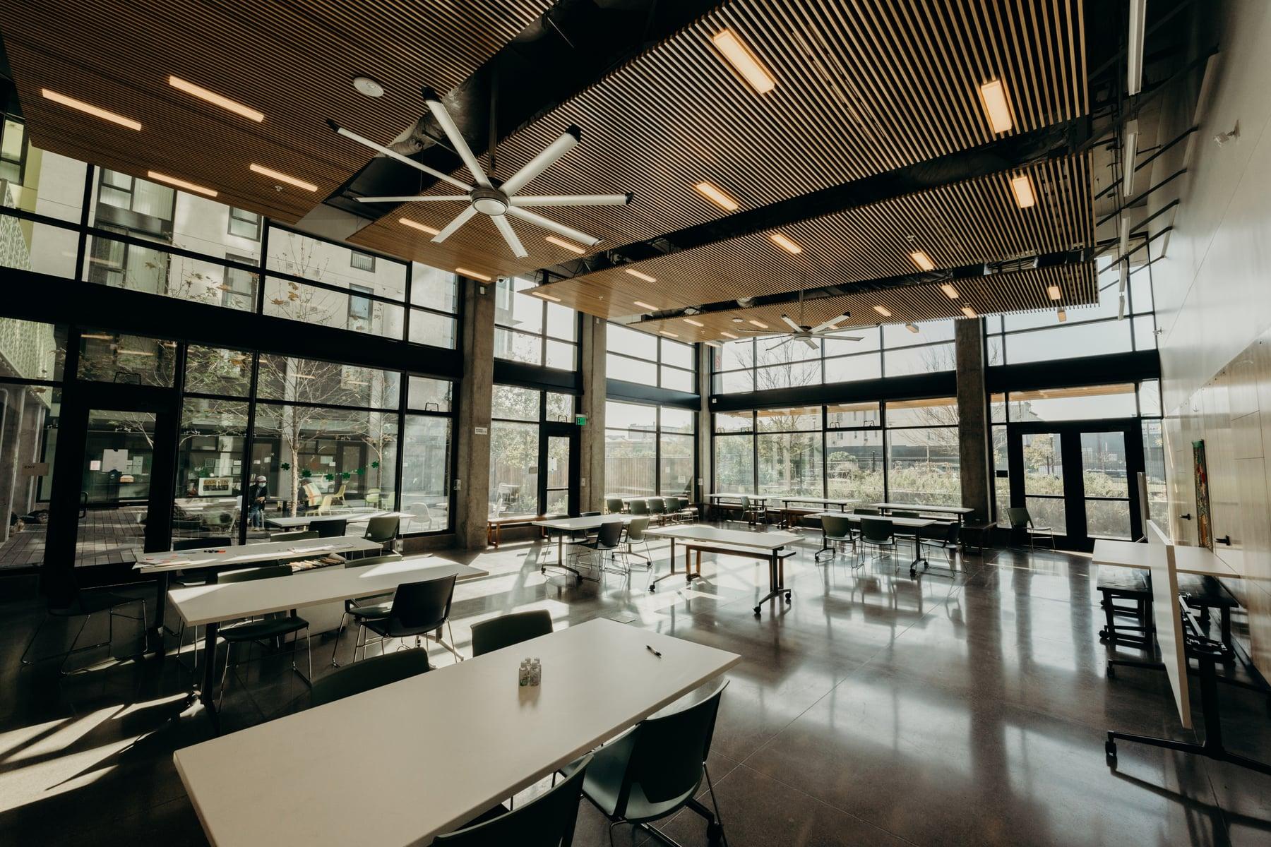 Community room with a wood-slat ceiling, tall black-framed glass walls and long tables