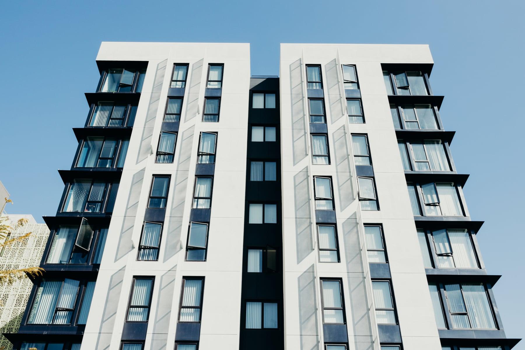 Two white-paneled residential wings with dark-framed windows and a darker center section under blue sky