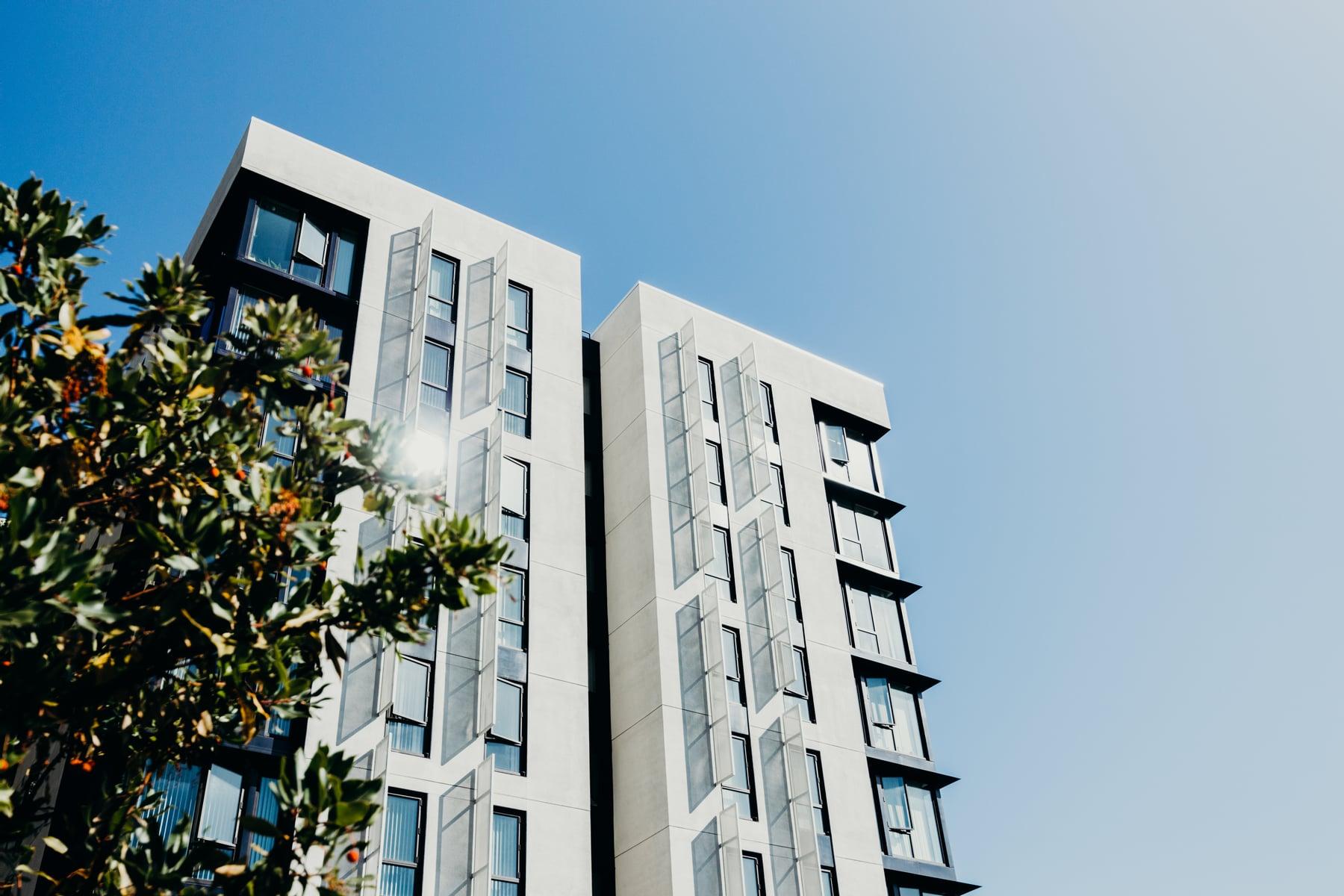Close view of a white building's tall bay windows with dark frames and gray panel strips, with foliage