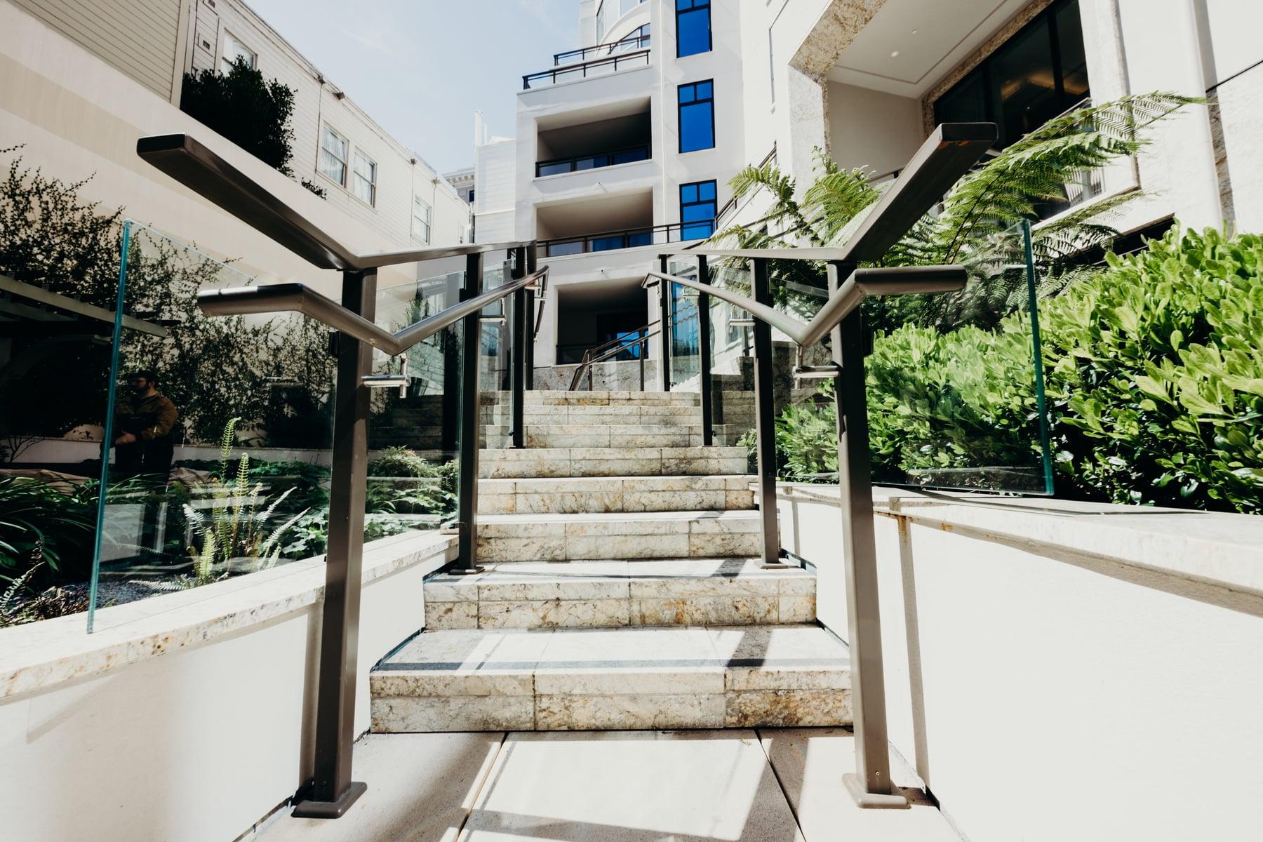 Steps with a dark metal handrail and glass panel between planting beds
