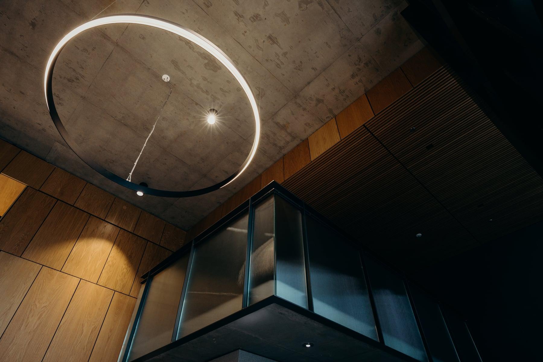 Ring-shaped light fixture beneath a wood-slat ceiling, with a glass-enclosed balcony edge
