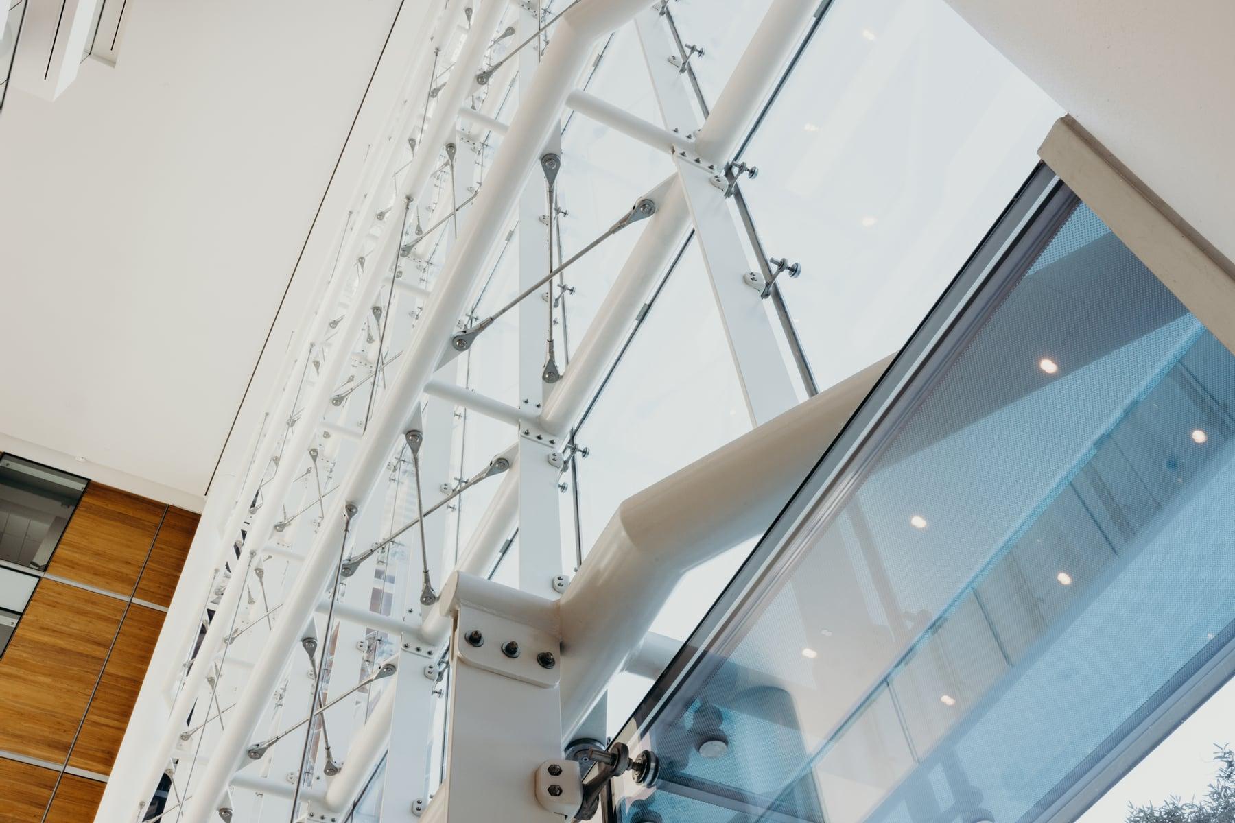 Close view of white steel supports, thin rods and connectors behind a tall glass wall
