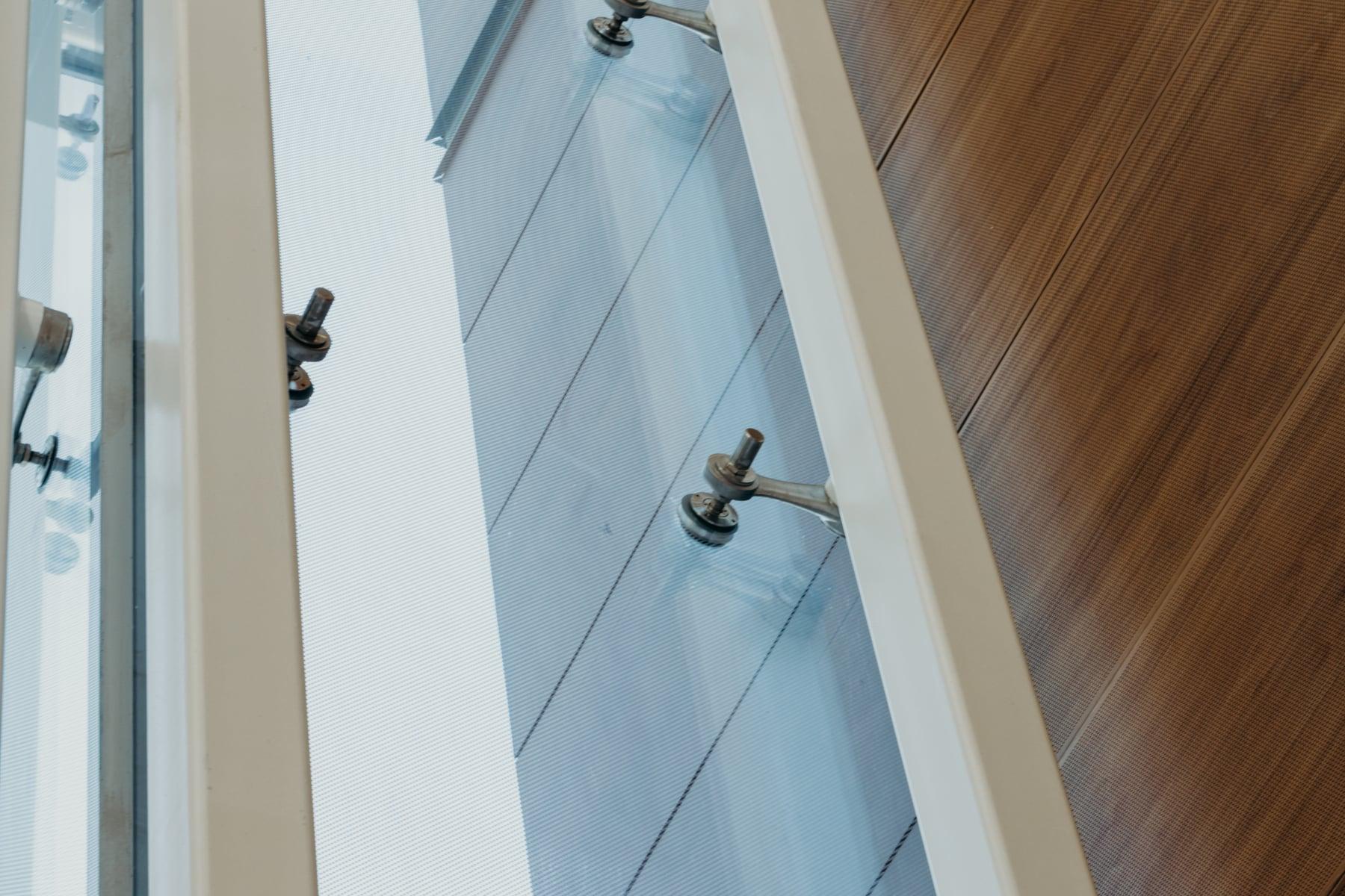 Detail of glass panels held by metal point fittings beside a wood-paneled wall