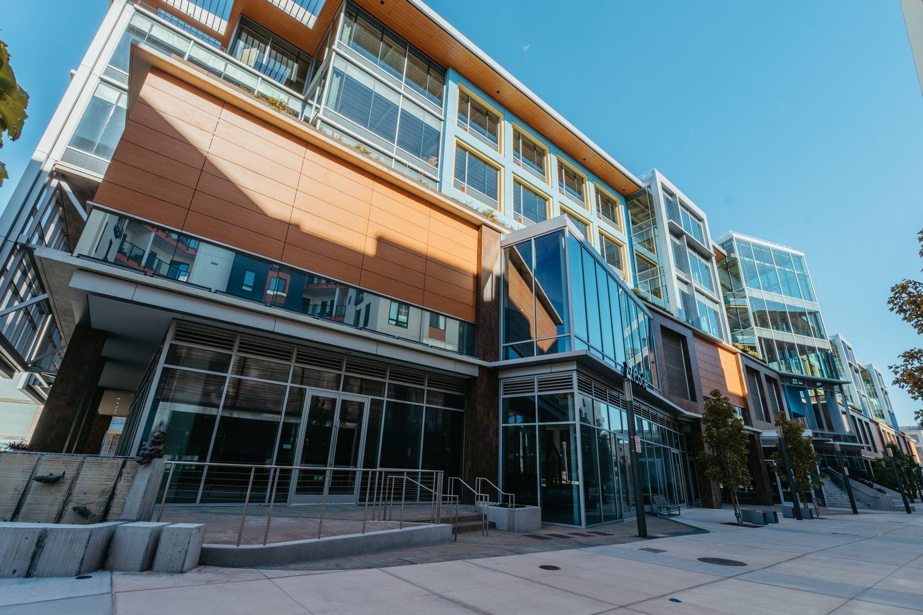 Street-level glass storefront of the Millbrae building below a wood-toned panel, with glazing on the upper floors