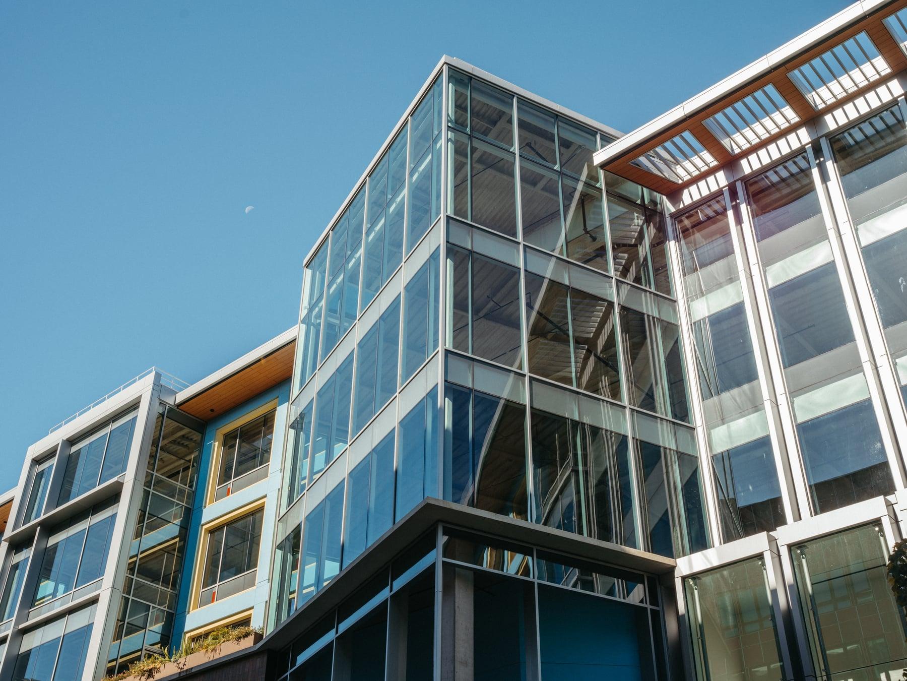 Looking up at glazed corner bays with blue and yellow framed windows and a louvered roof overhang