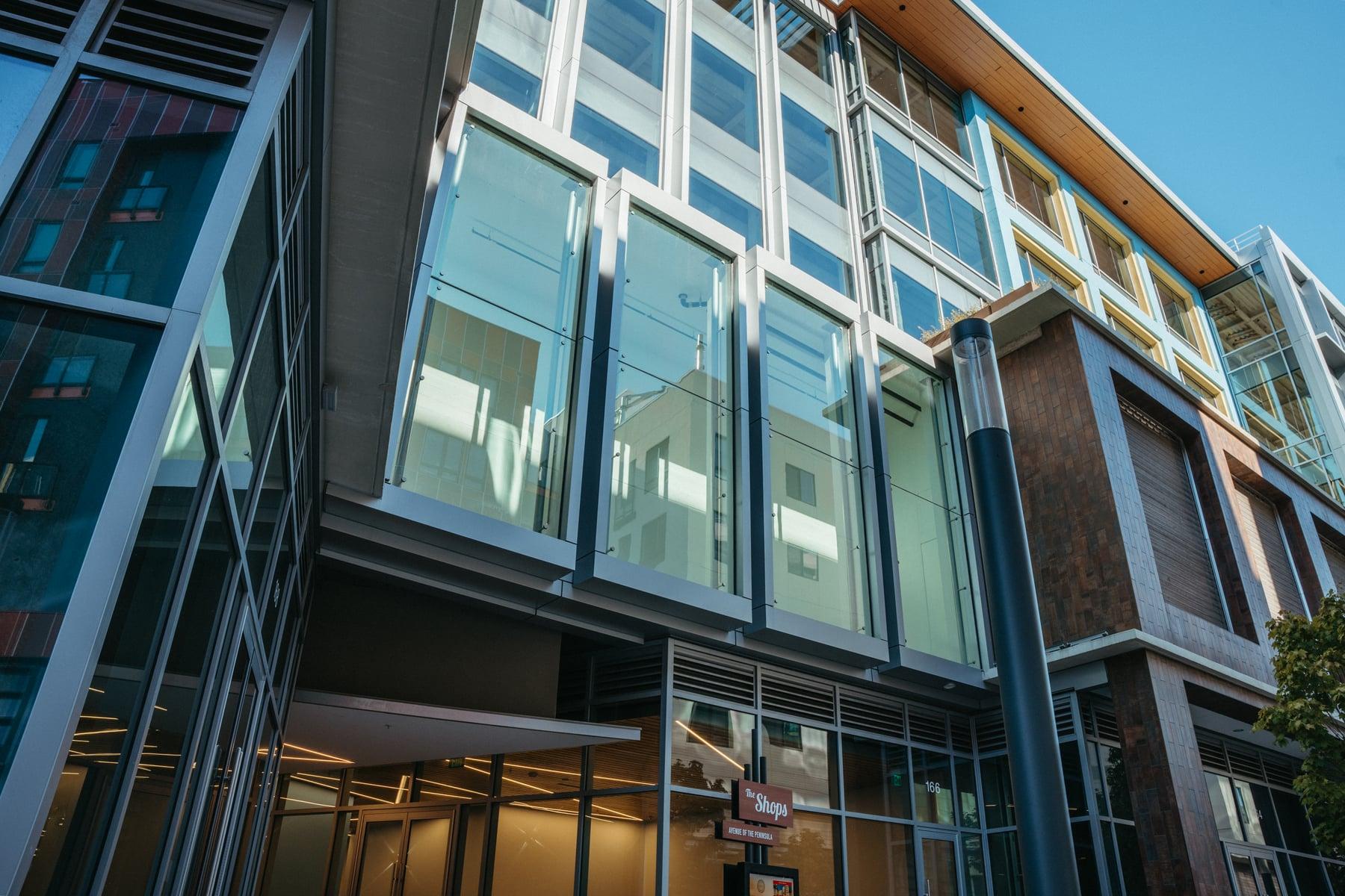 Close view of tall glass panels in metal frames on the upper floors, with a dark column and wood-toned soffit above