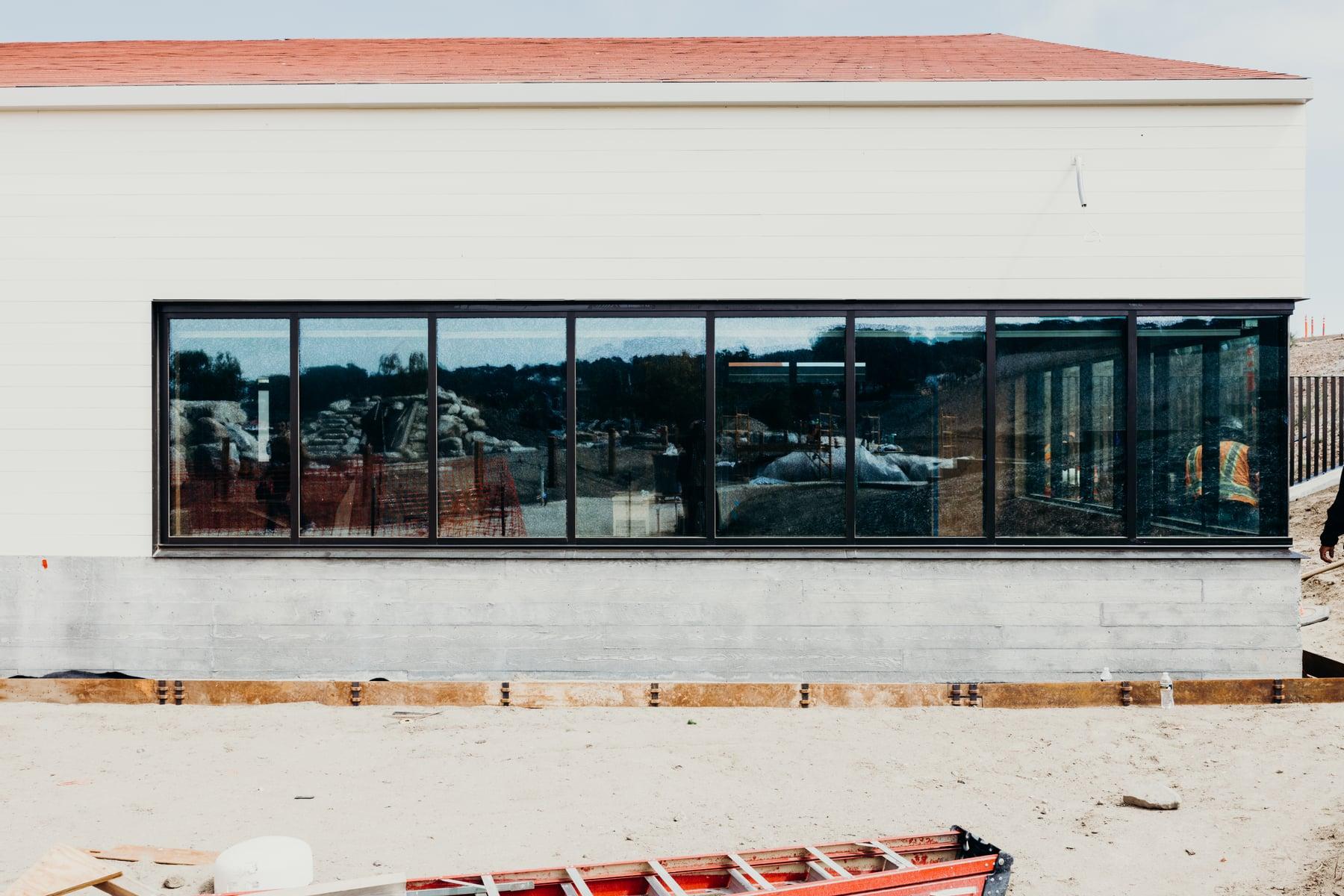 Long black-framed ribbon window on a white building wall at a construction site, with a ladder in the foreground