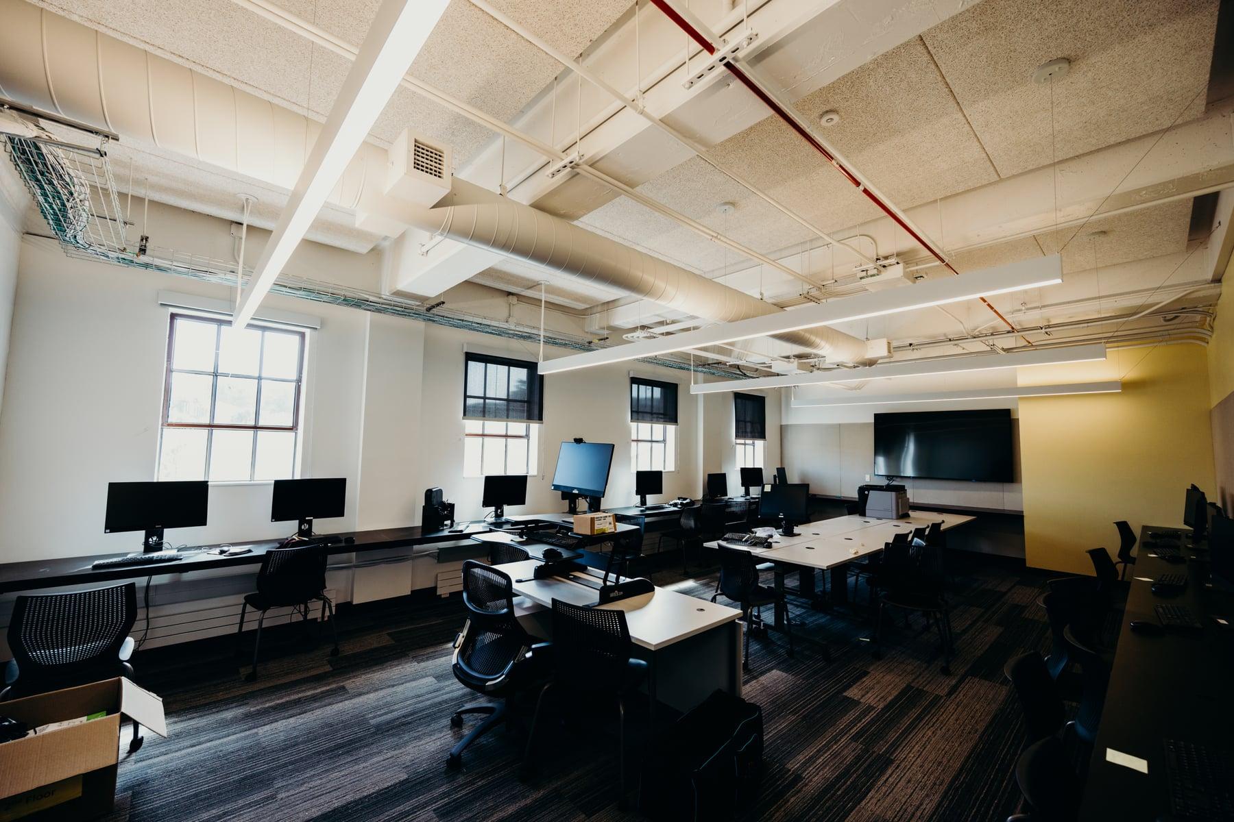 Interior office with white-framed windows, desks with computer monitors and exposed ceiling ducts