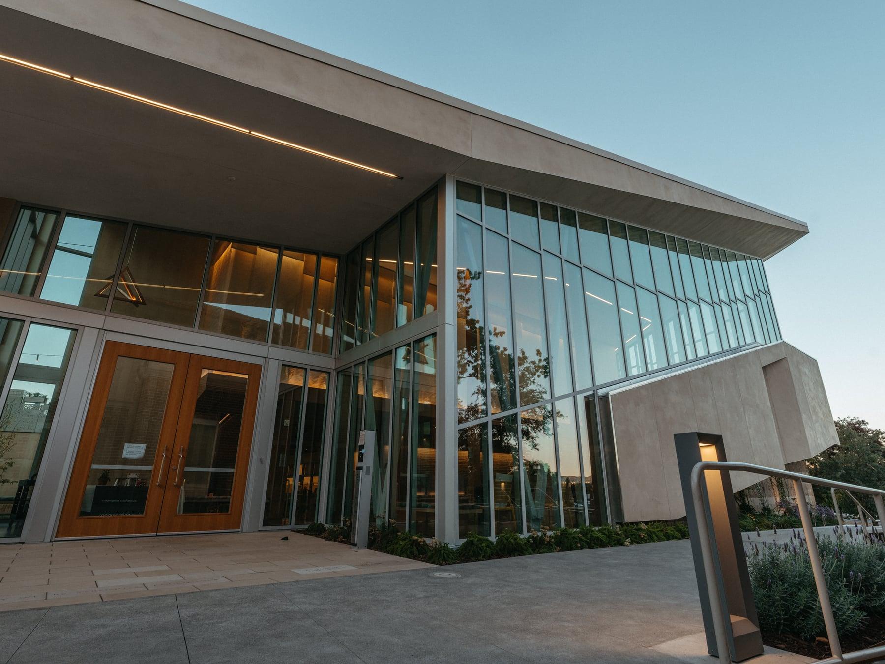 Entrance corner of Congregation Rodef Sholom with wood-framed double doors and a tall glass wall under a projecting roof
