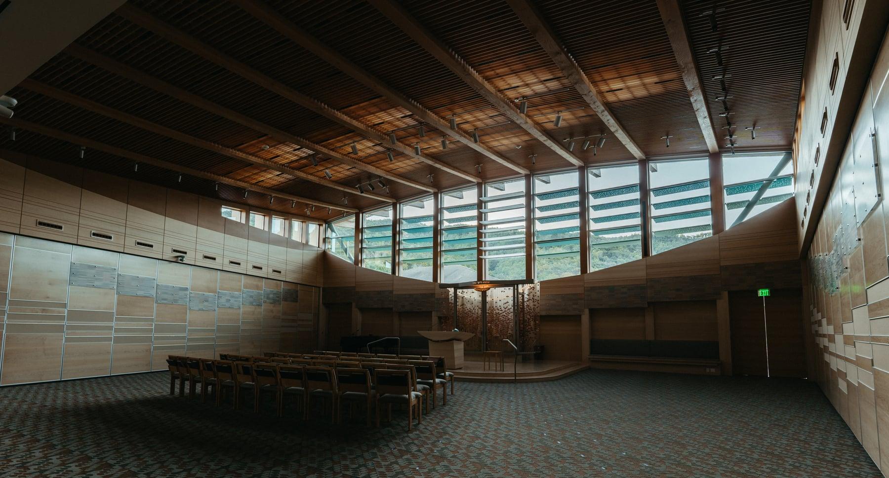 Interior hall with wood ceiling beams, a continuous band of high windows and rows of chairs