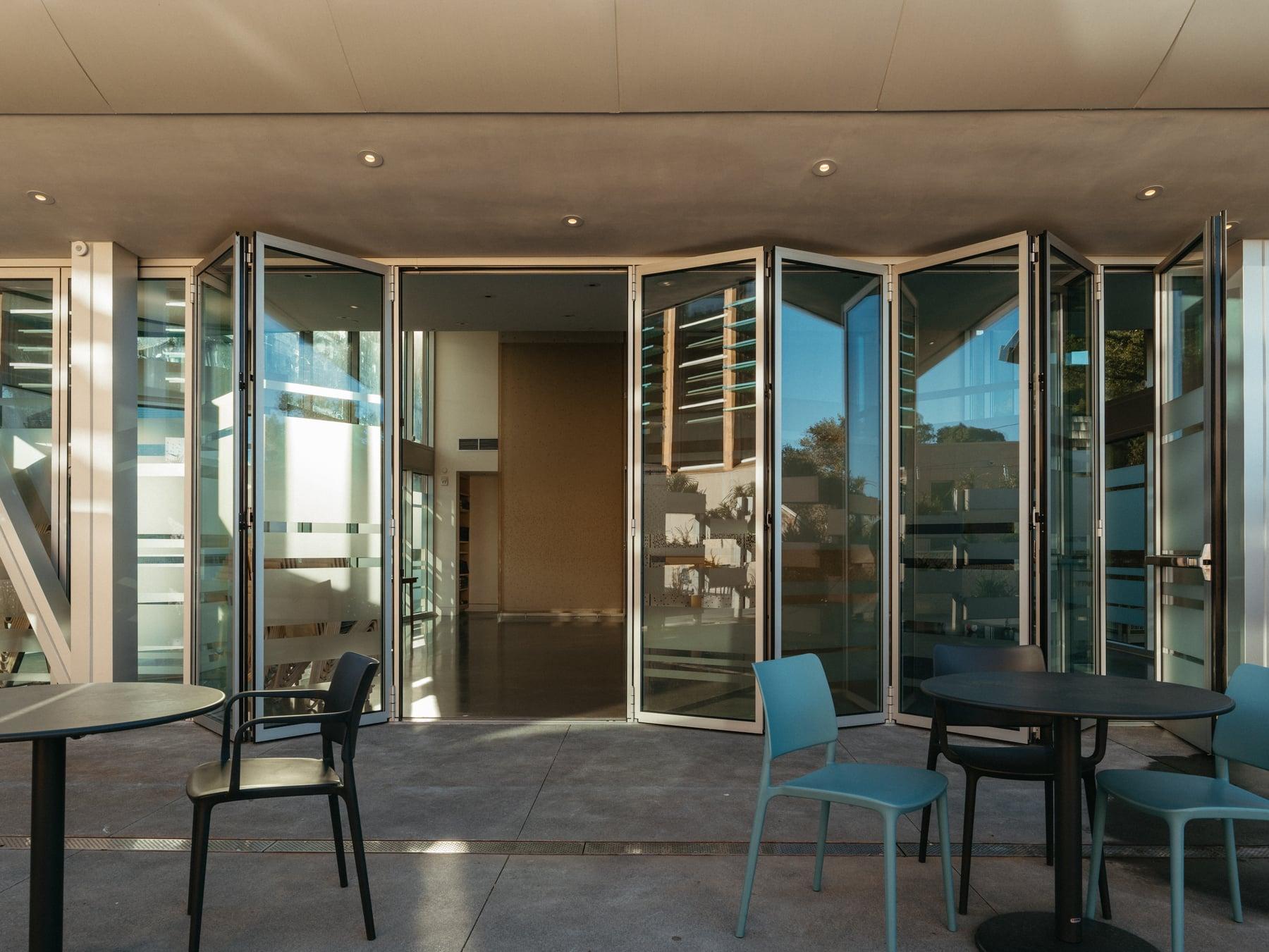 Folding glass wall opened onto an outdoor patio with tables and chairs