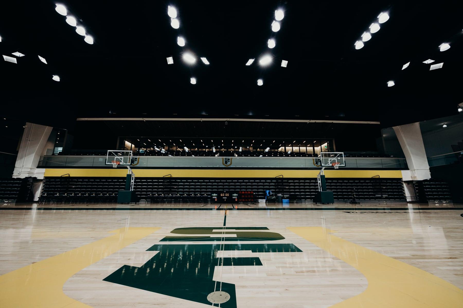 Basketball court at USF War Memorial Gymnasium with a green and gold center logo, seen from the sideline under arena lighting