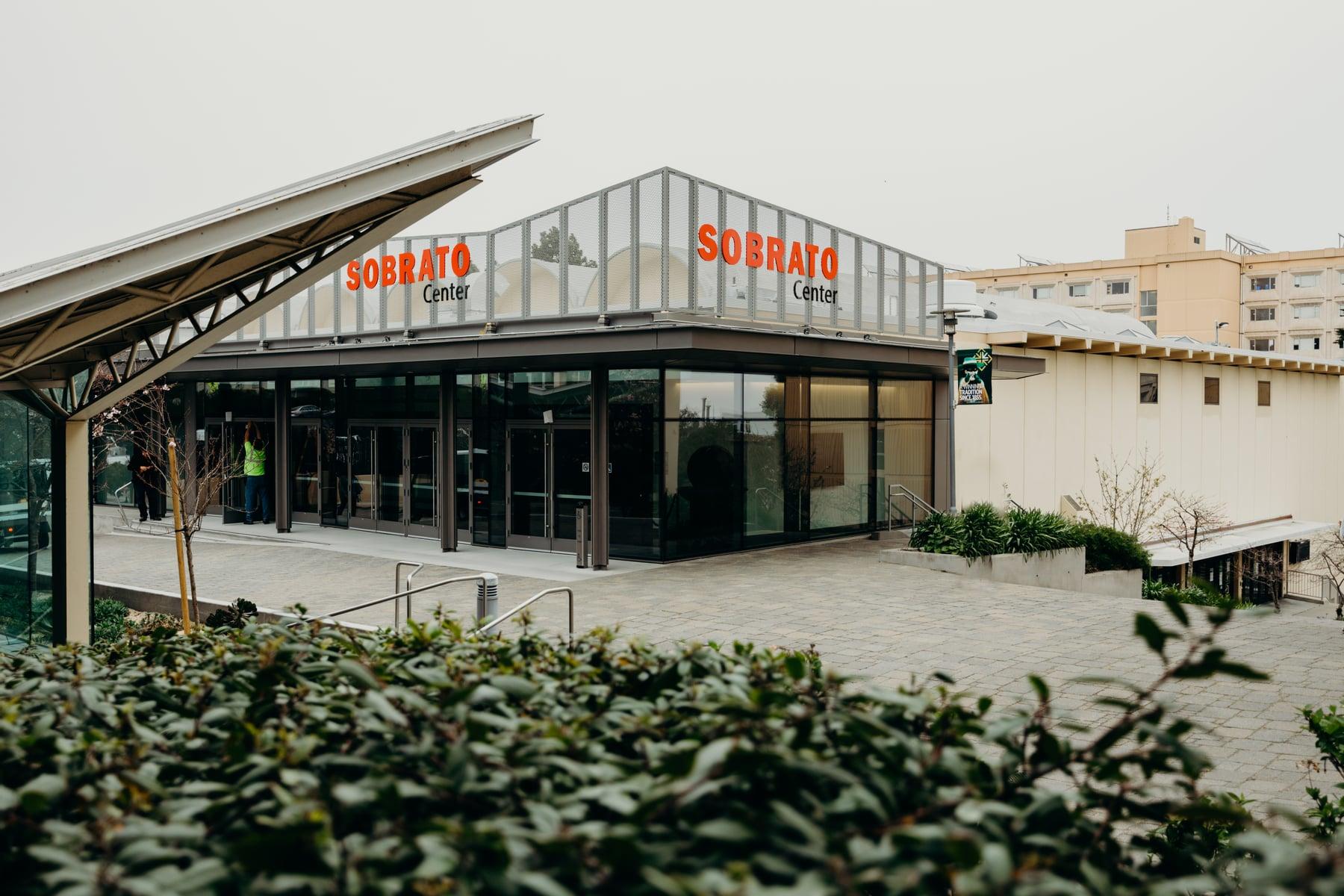Glazed entrance building of the Sobrato Center at USF, with red lettering, across a paved plaza
