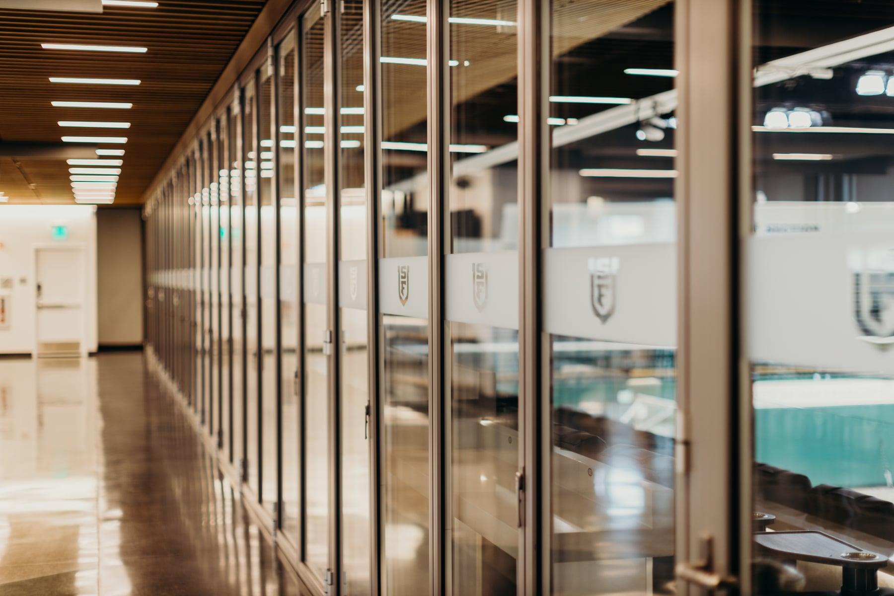 Long row of glass panels along the gymnasium concourse, with frosted USF crest graphics and the court beyond