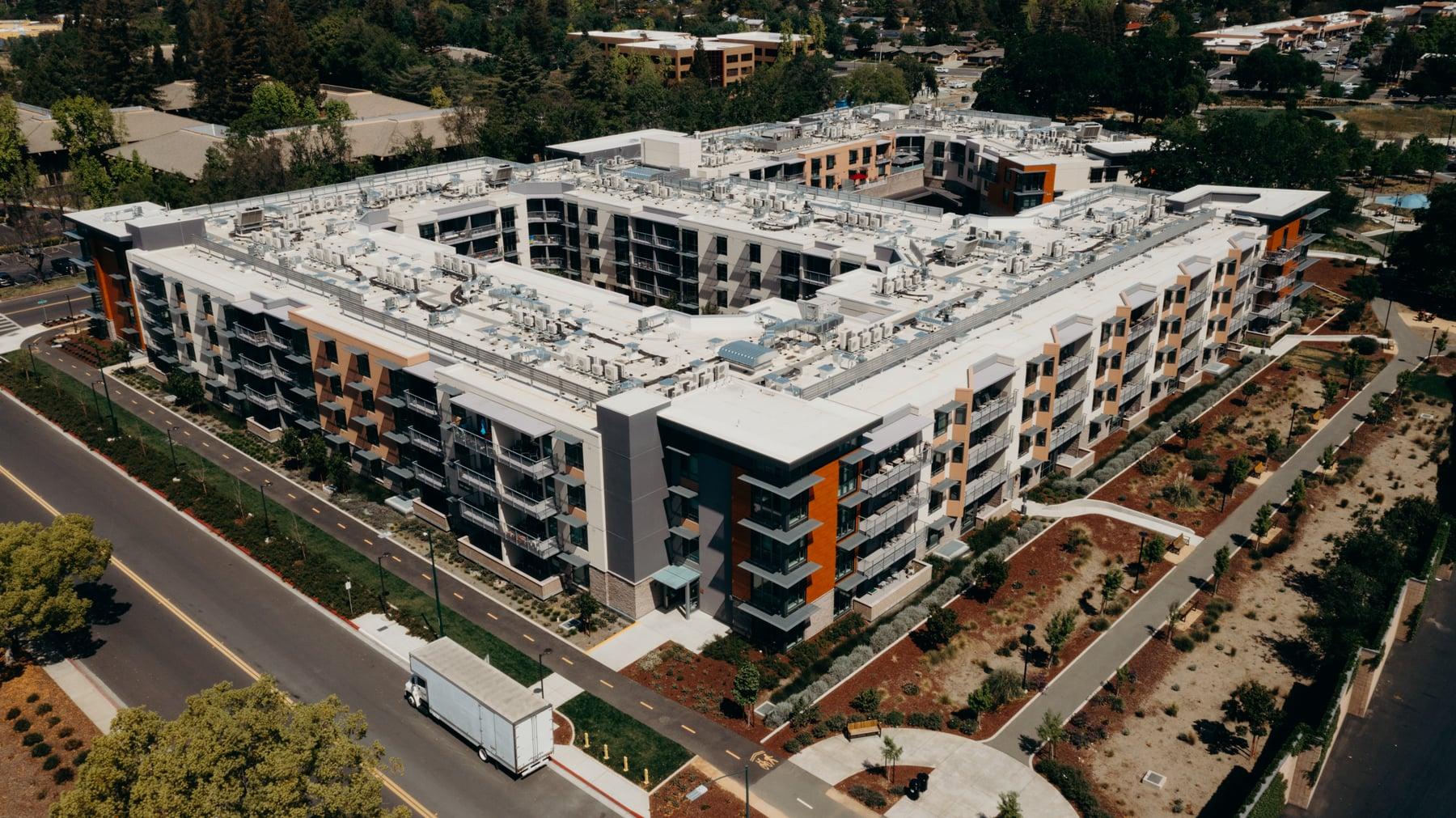 Aerial view of the courtyard-style apartment building with surrounding landscaping and a road