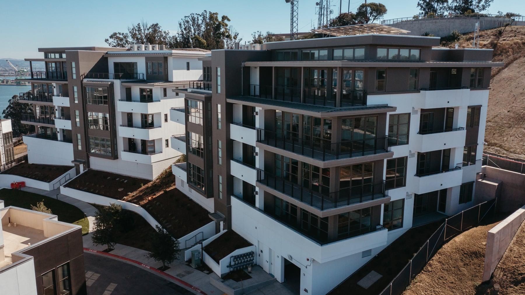 Residential building with rows of balconies and large windows on a sloped site under blue sky