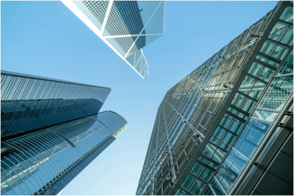 Upward view between two modern glazed skyscrapers, reflecting sunlight against a clear blue sky.