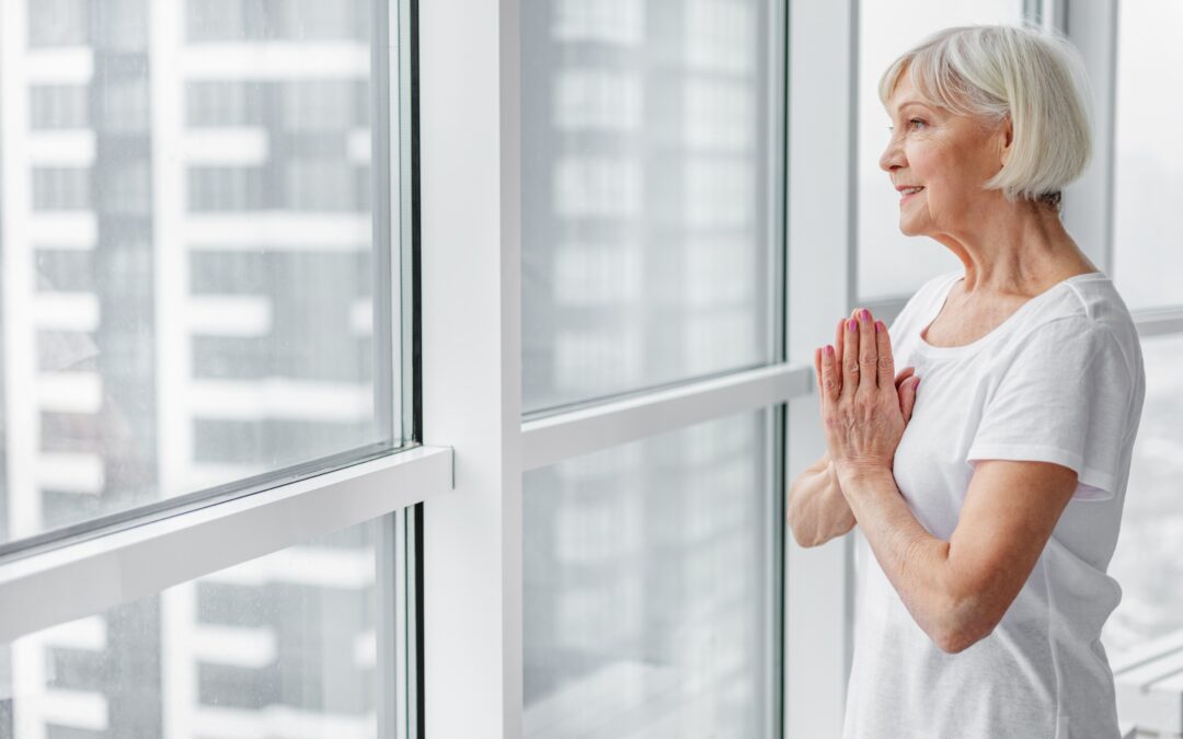 A woman standing near large clear windows in a high-rise building, gazing out at a city skyline, reflecting a sense of openness and perspective.